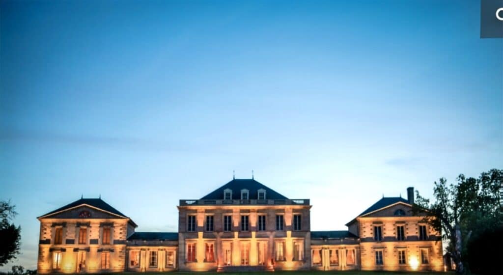 Château français illuminé au crépuscule, architecture symétrique sous un ciel bleu.
