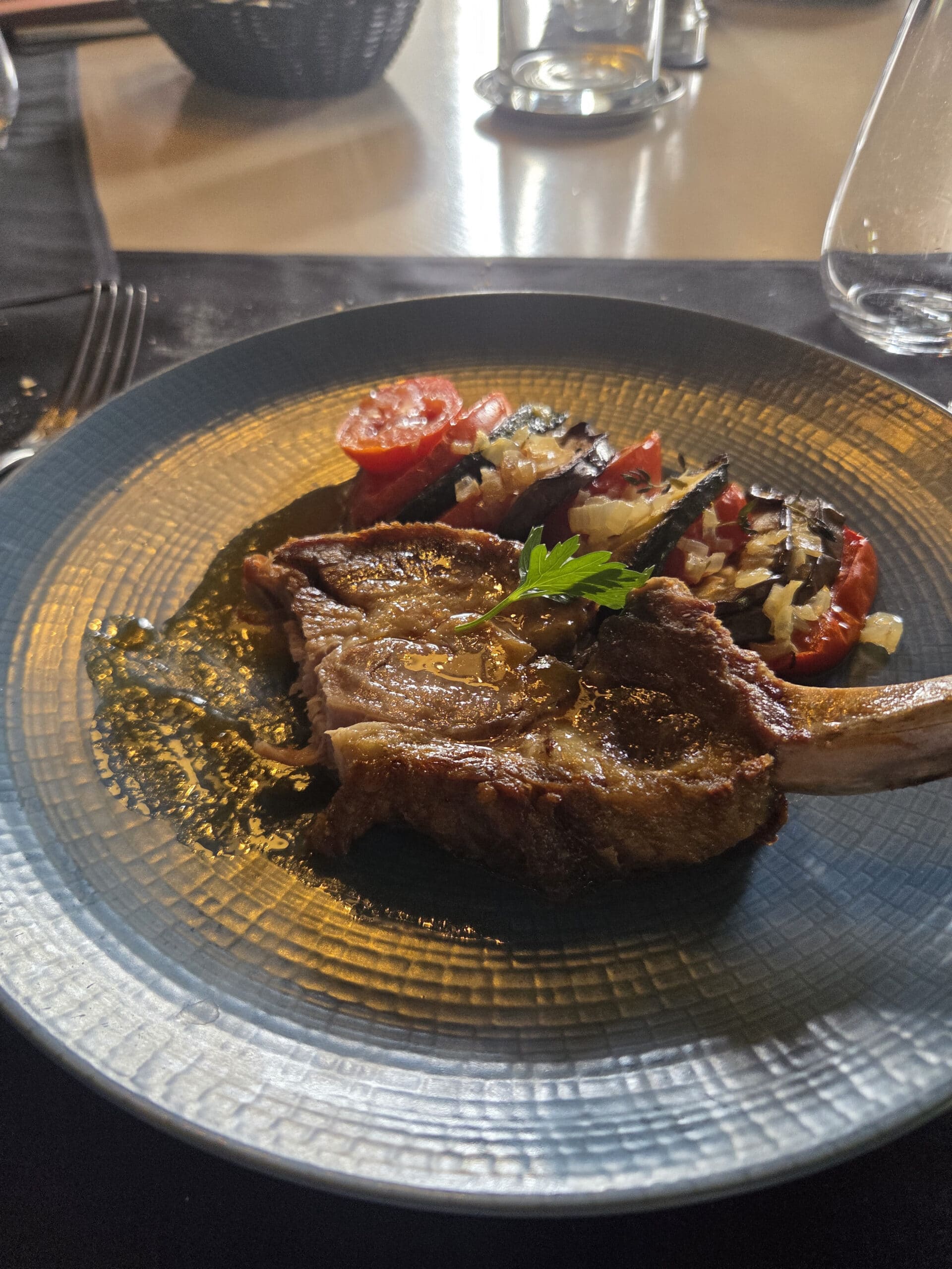 Côte de viande rôtie et ratatouille sur assiette bleue, décor de restaurant élégant.