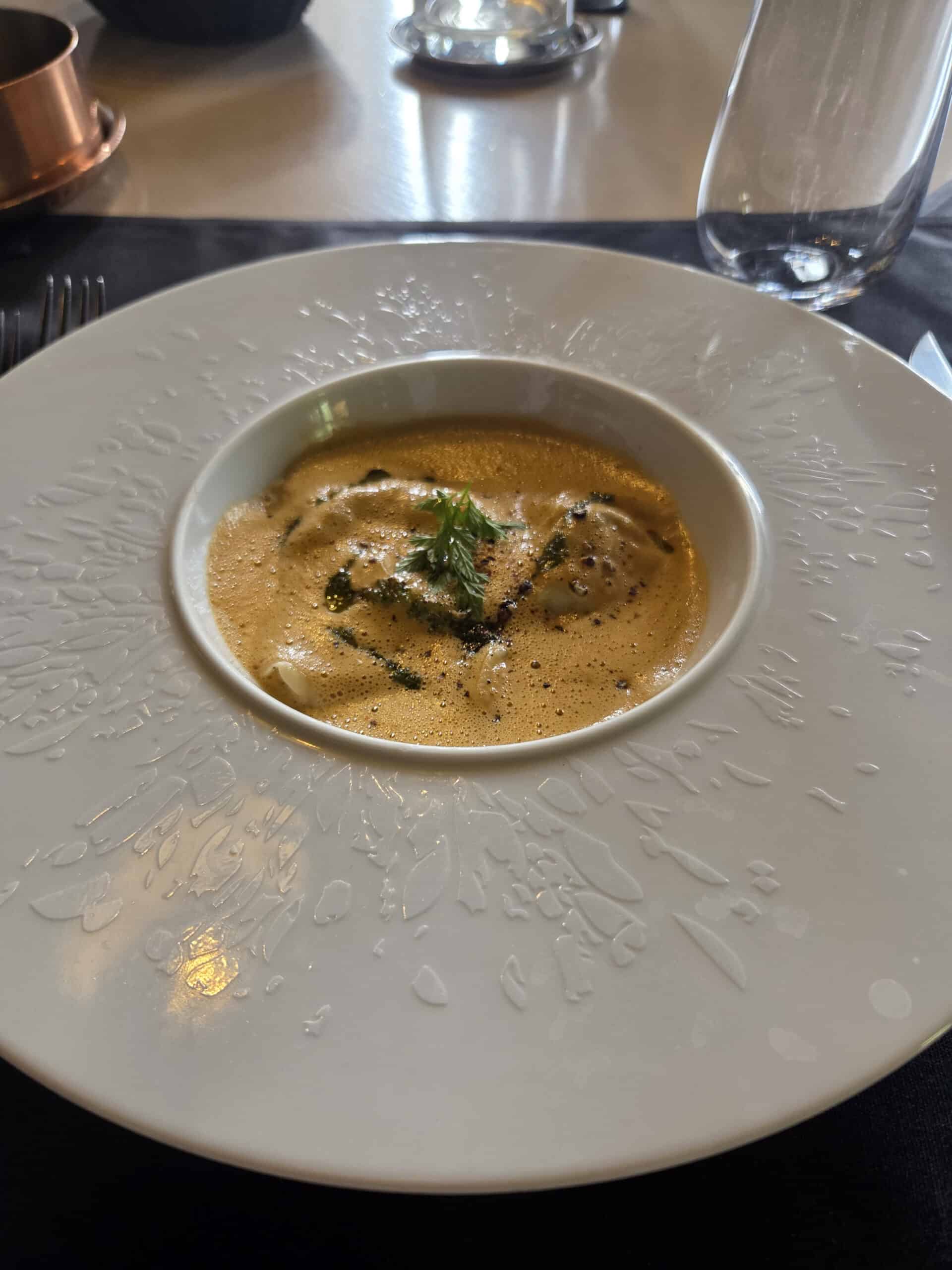 Soupe onctueuse et herbes fraîches dans une assiette blanche à motifs texturés.